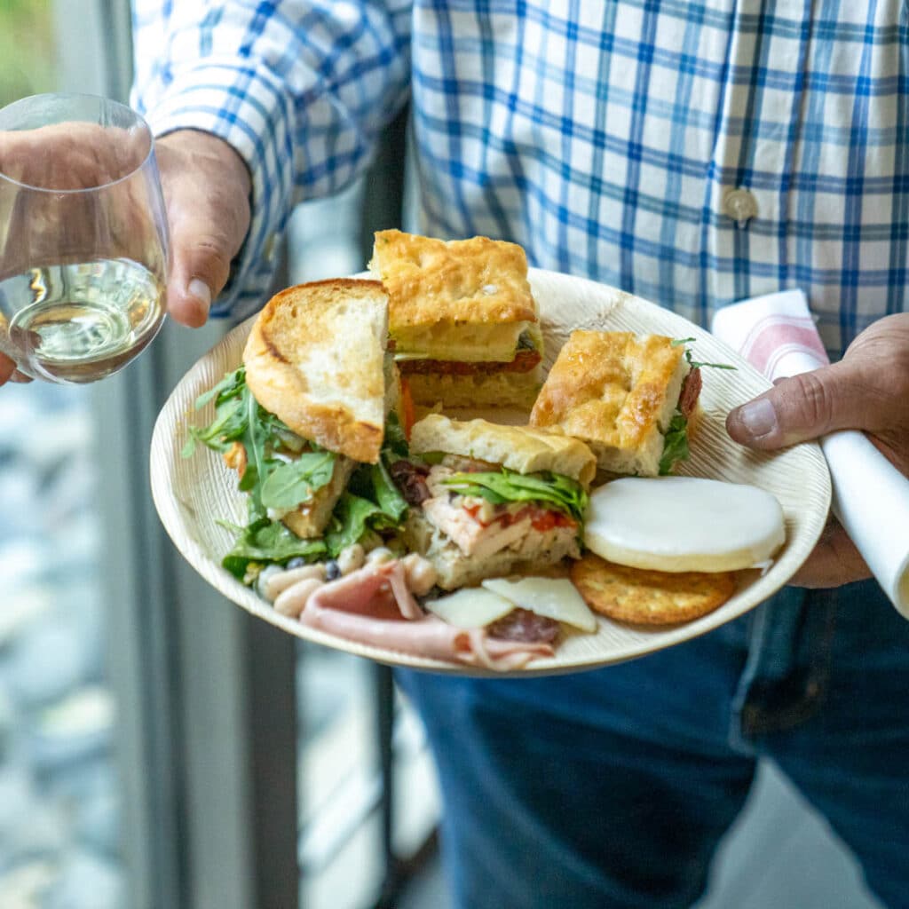 Hands holding a plate of food and a glass of wine from Frascati Market