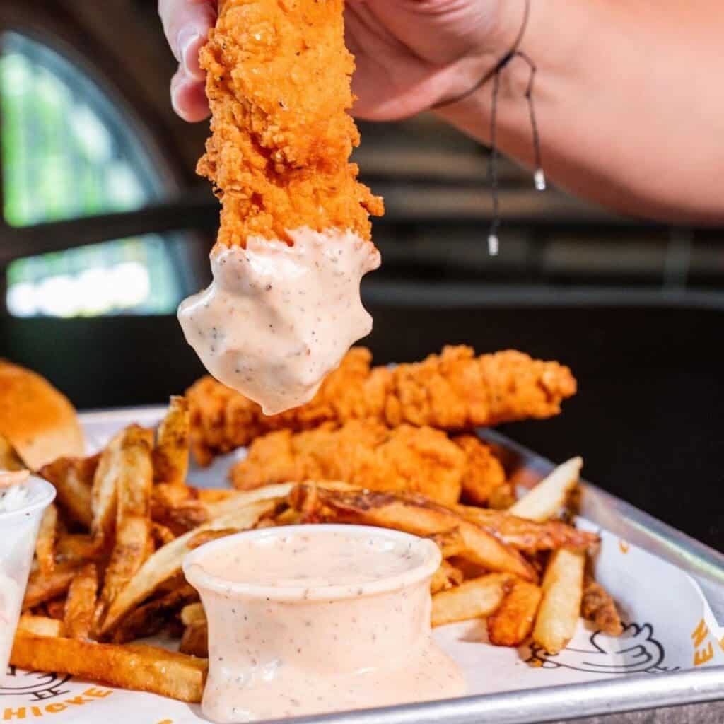 A chicken tender being dunked in a tub of sauce