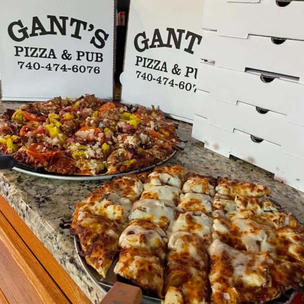 Two pizzas from Gant's Pizza with delivery boxes in the background