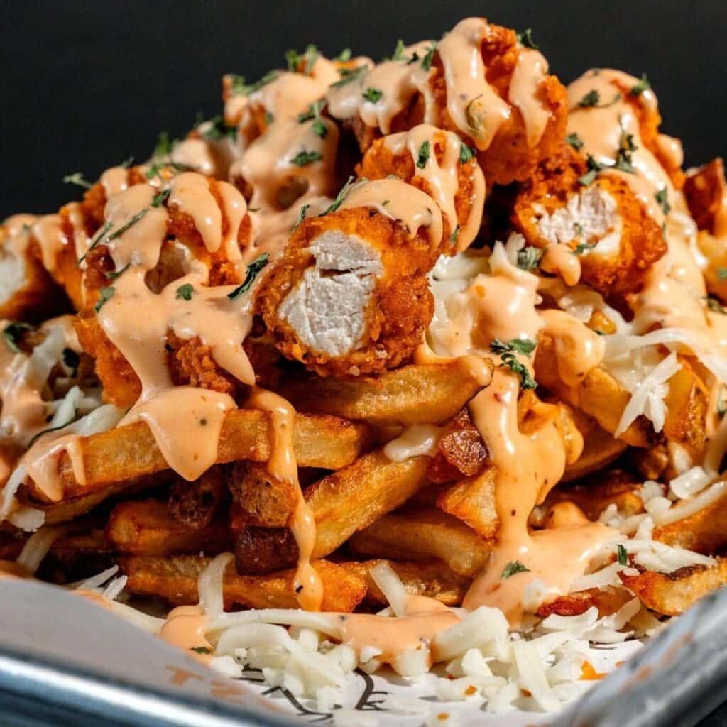 A plate of fries topped with chicken tenders and sauce from Just Chicken