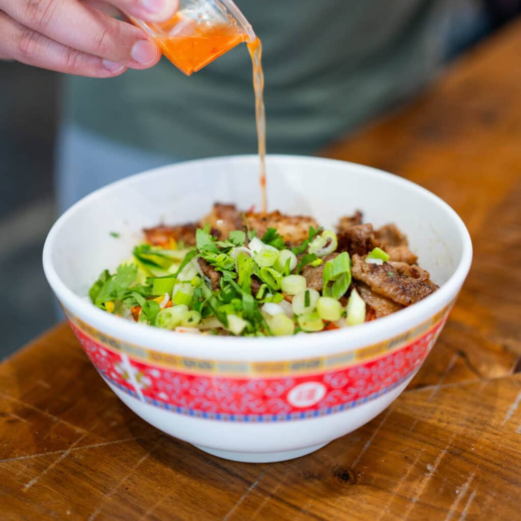 A stir fry bowl from Lan Viet with a hand pouring sauce over.