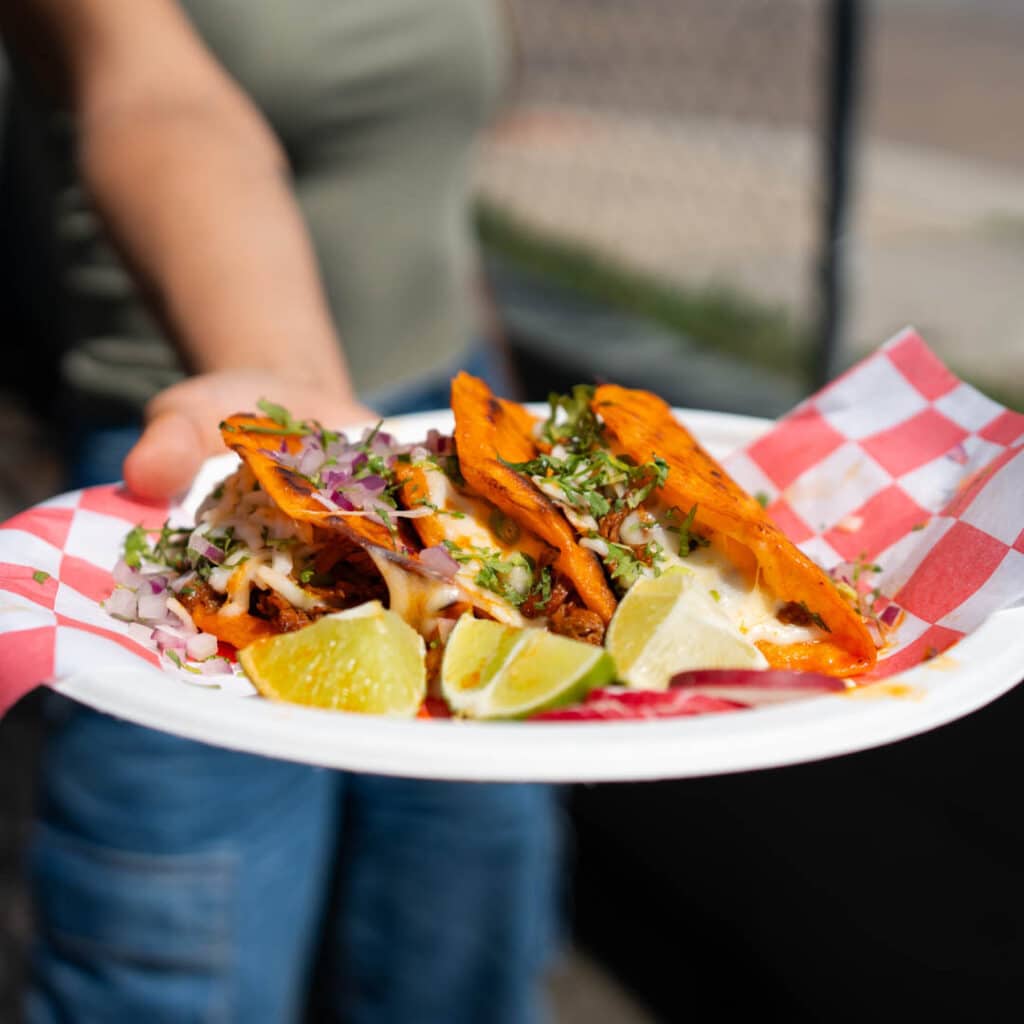 A hand extending a plate of tacos from Los Agavez